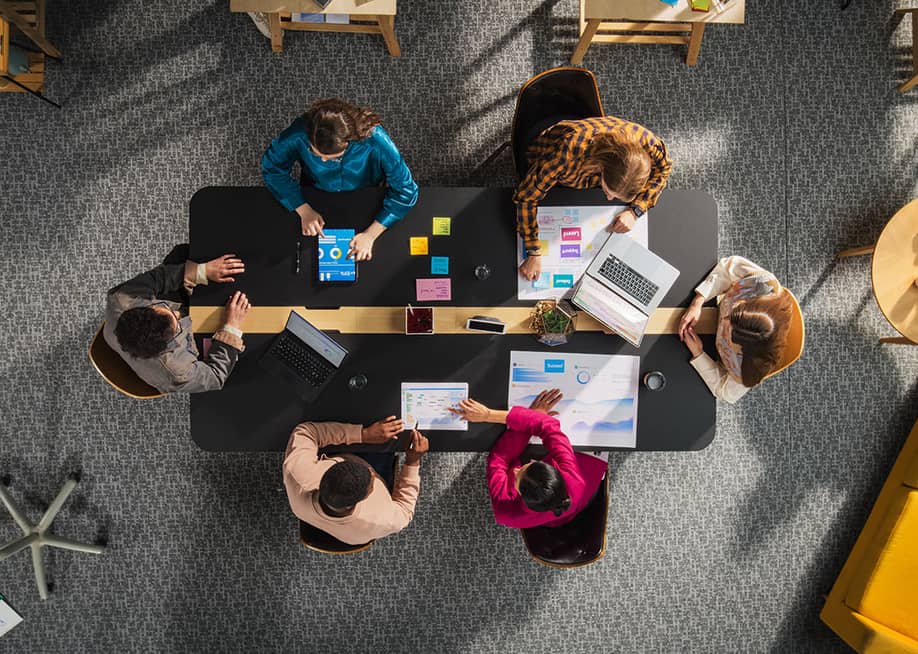 Top view of a team of entrepreneurs seated around a table in a meeting room. — Gorodenkoff // Shutterstock