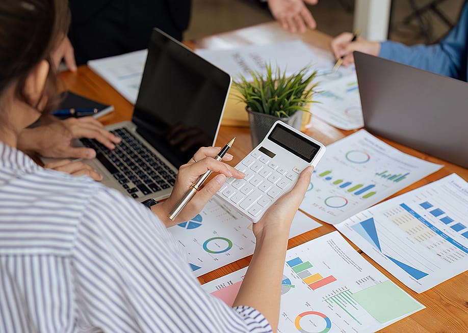 Businesswoman using a calculator while reviewing reports. — Worawee Meepian // Shutterstock