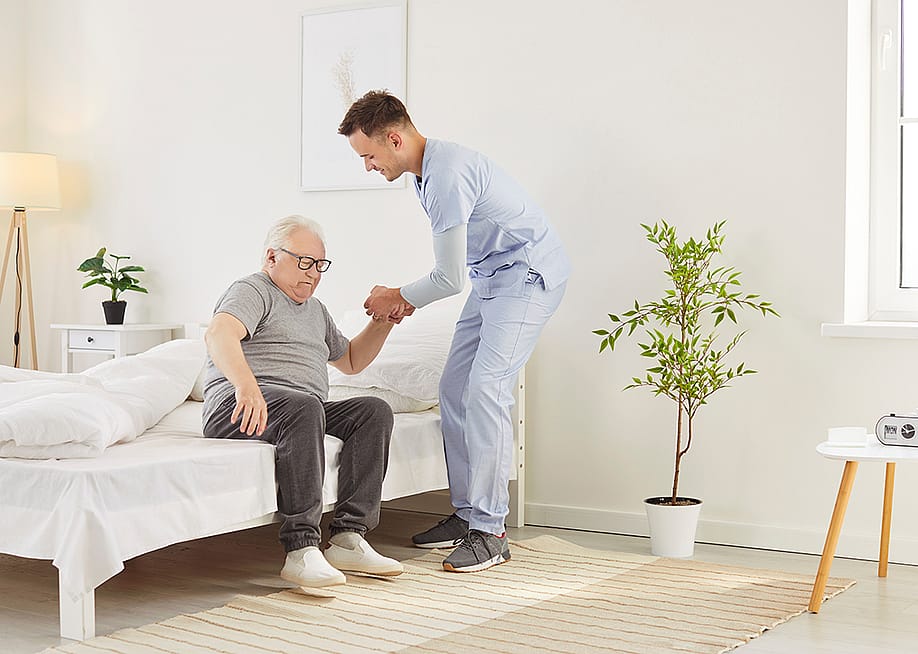 A nurse helping an elderly patient get out of bed in a nursing home. — Studio Romantic // Shutterstock