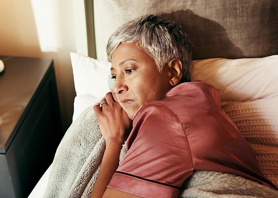 A middle-aged woman lying in bed in deep thought. — PeopleImages // Shutterstock