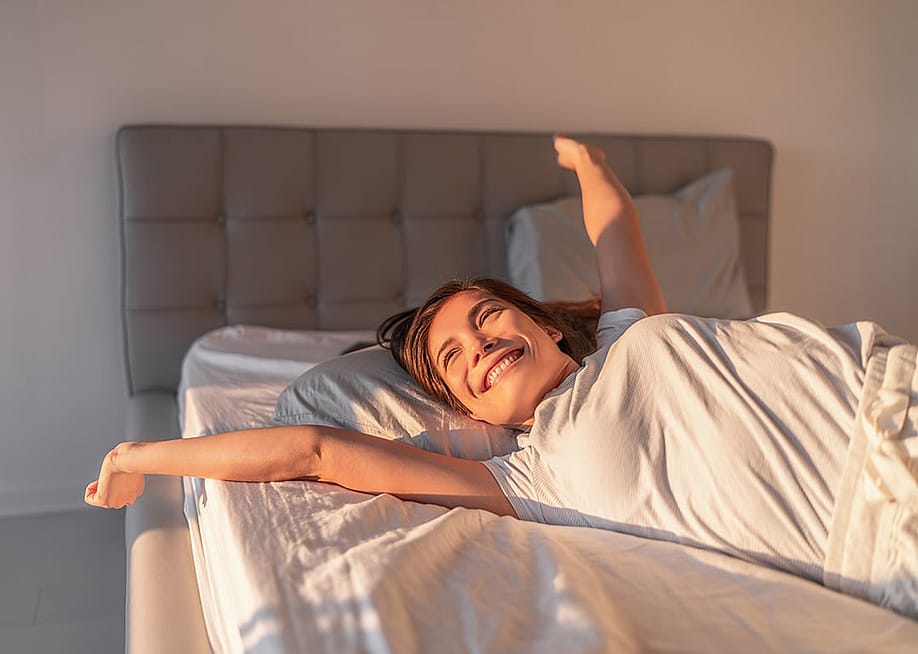 A happy young woman waking up in the morning. — Maridav // Shutterstock