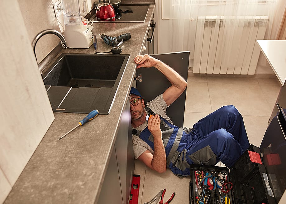 A plumber fixing a water pipe under the kitchen sink. — AstroStar // Shutterstock