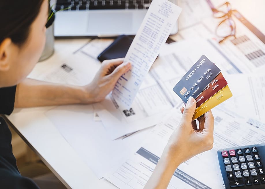 Woman looking at multiple credit cards and calculating debt expenses. — Pormezz // Shutterstock