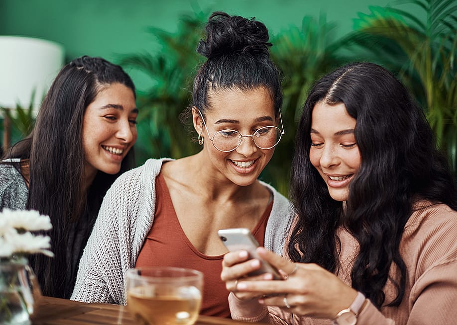 Friends checking social media in a cafe. — PeopleImages // Shutterstock