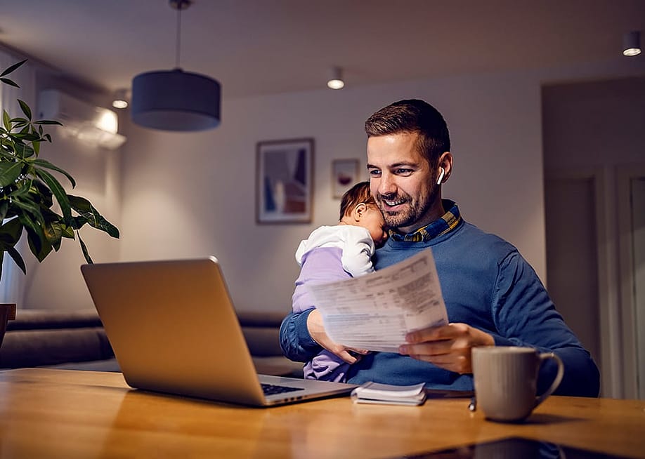 A young father carrying his baby asleep while working remotely from home. — Dusan Petkovic // Shutterstock