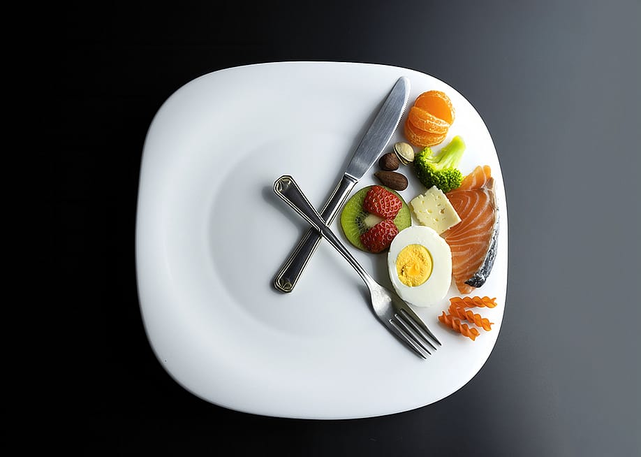 A plate of healthy ingredients simulating a clock with its hands represented by a knife and a fork as a concept of intermittent fasting. — Sendo Serra // Shutterstock