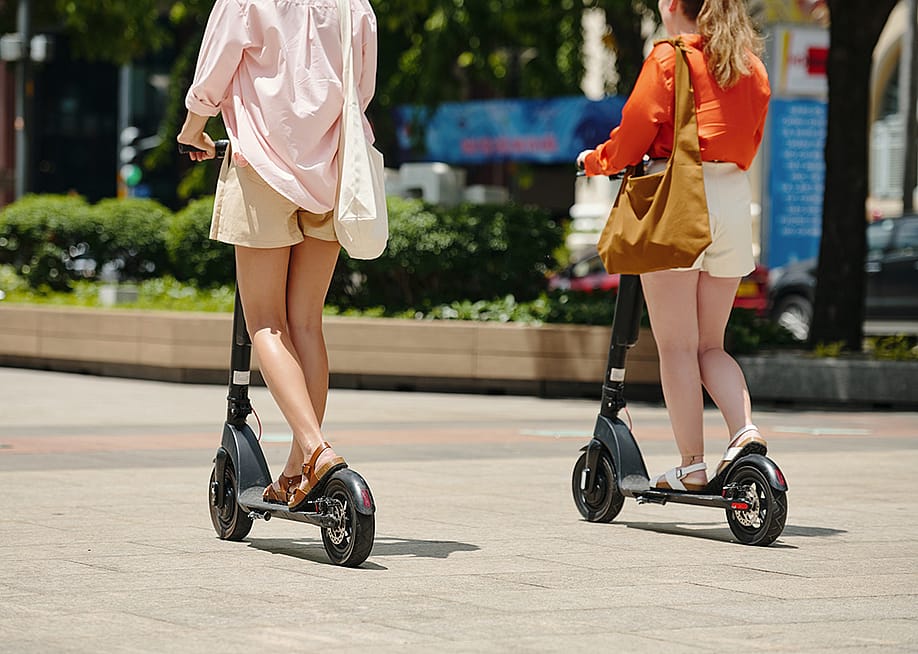 Two women riding electric scooters outdoors. — Dragon Images // Shutterstock