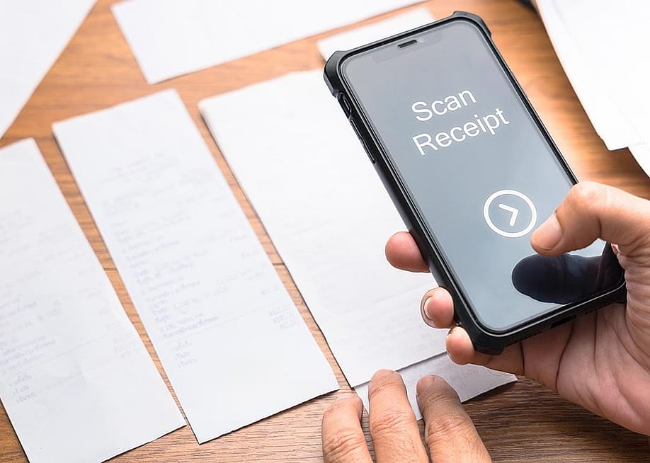 A person scanning paper receipts from a smartphone. — patpitchaya // Shutterstock