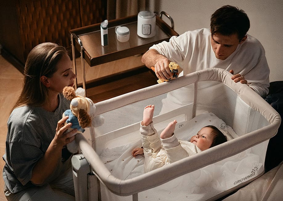 Parents entertaining their baby in a crib with toys. — GROWNSY