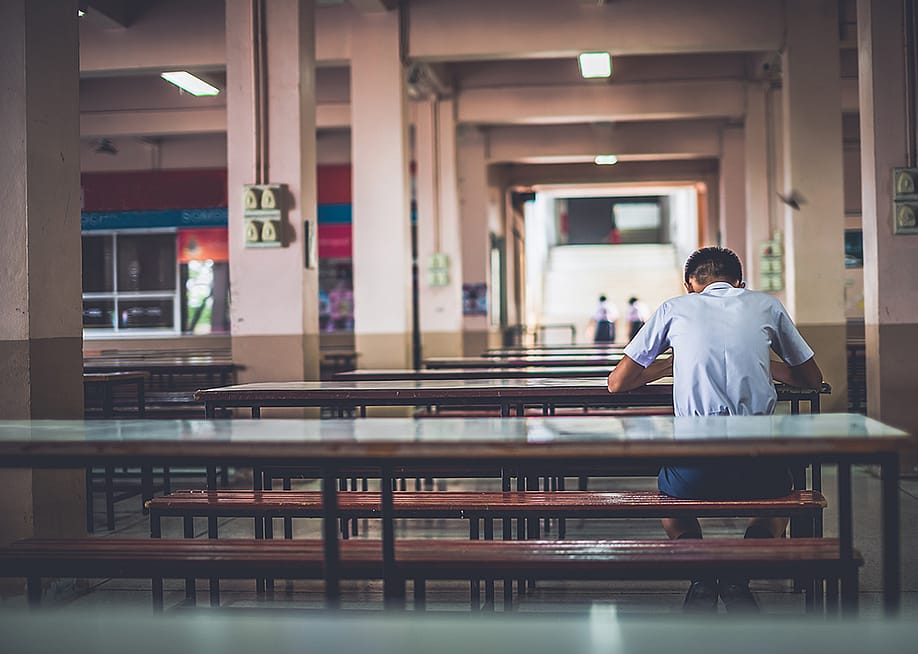 A male high school student sitting alone at a cafeteria. — POP-THAILAND // Shutterstock