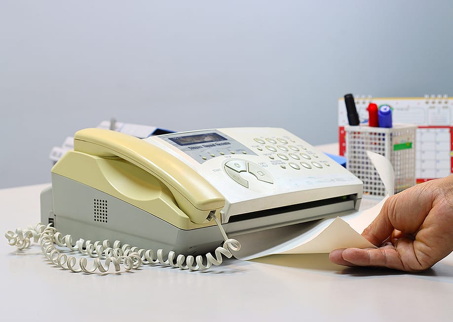 Person feeding a yellowing fax machine paper. — junpiiiiiiiiiii // Shutterstock