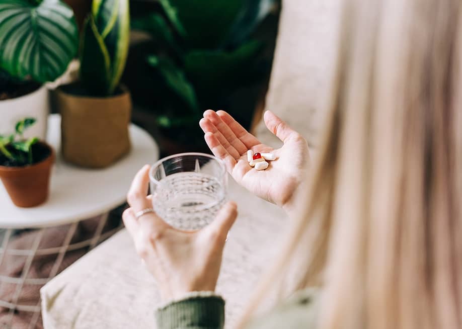 A woman holding multiple pills to drink with a glass of water. — Ostanina Anna // Shutterstock