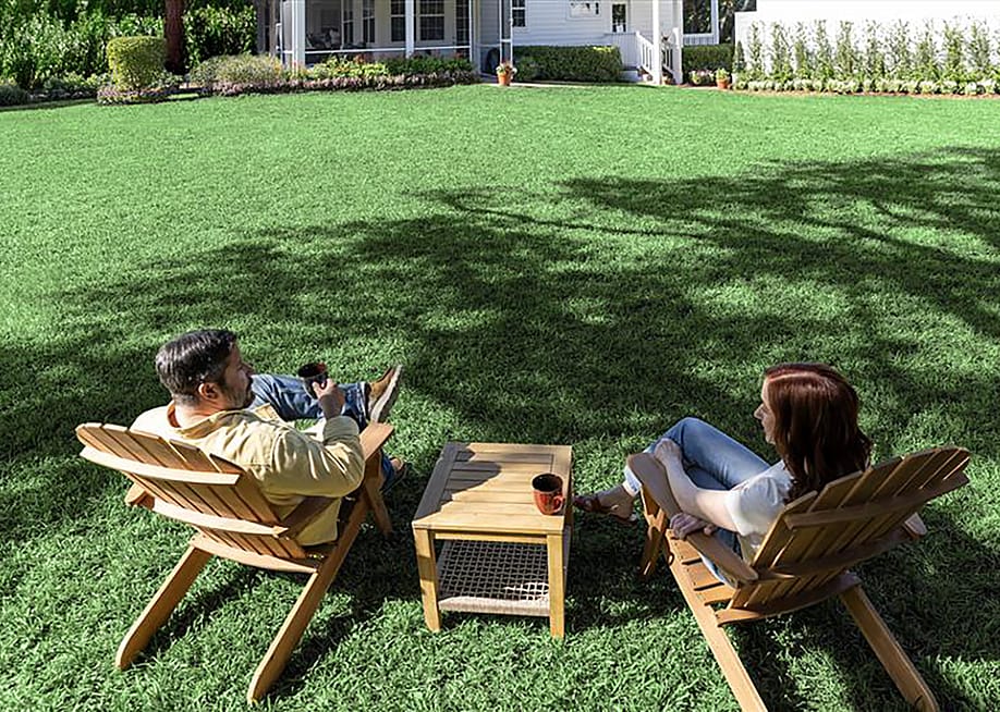 A couple sitting under the shade of trees in their backyard. — TruGreen