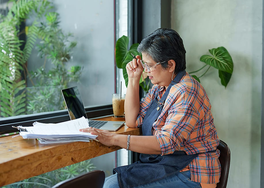 A senior small businesswoman reviewing reports by the window of her store. — Ekkasit A Siam // Shutterstock
