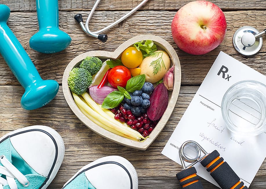 Fruits and vegetables in a heart bowl surrounded by fitness and healthy lifestyle objects. — udra11 // Shutterstock