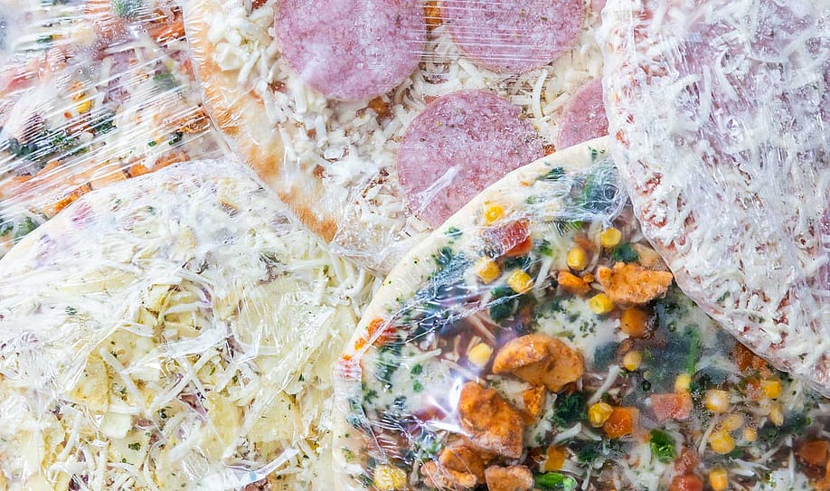Multiple frozen pizzas wrapped in plastic stacked on each other — Simon Kadula // Shutterstock.com