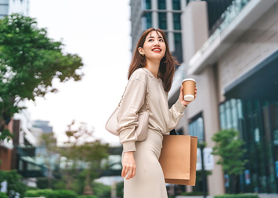 A young woman holding a cup of coffee and shopping bag outdoors. — dodotone // Shutterstock