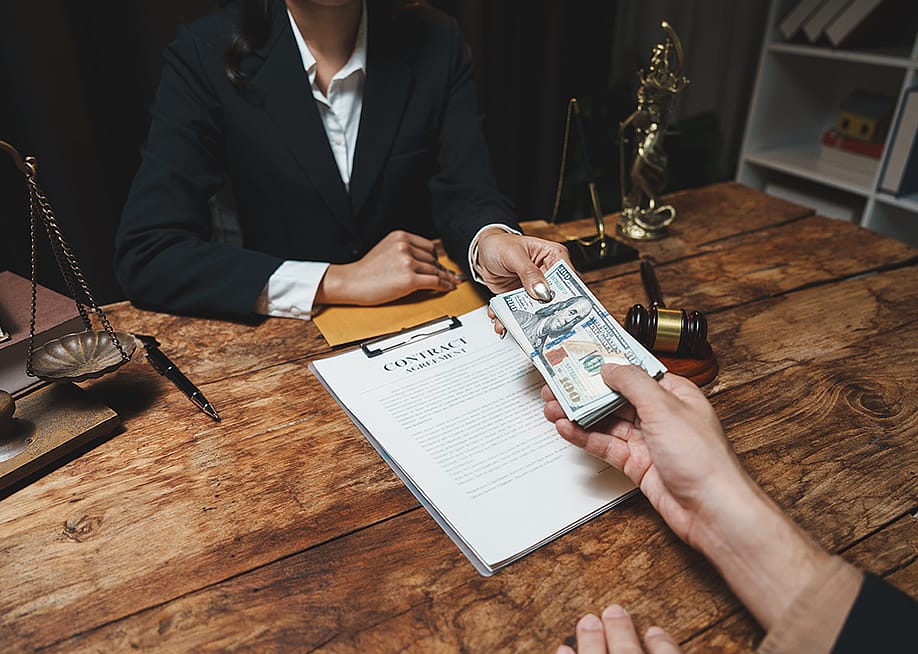 A legal professional accepting cash from a client over a contract agreement. — CrizzyStudio // Shutterstock