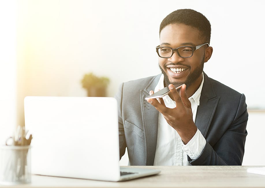 A happy young black businessman using voice assistant on his smartphone. — Prostock-studio // Shutterstock