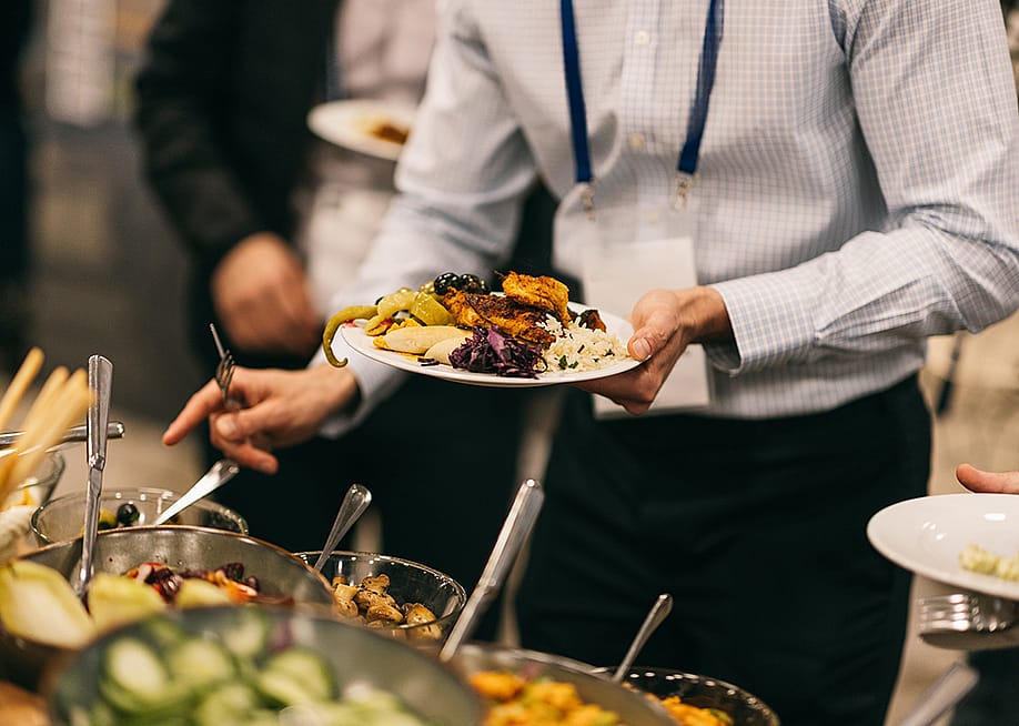 An employee holding up a plate of Mediterranean food from a catering event. — Power studio // Shutterstock