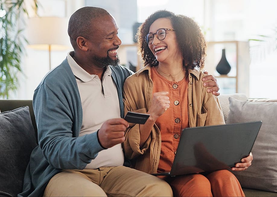 A happy couple at home purchasing online with a credit card. — PeopleImages // Shutterstock
