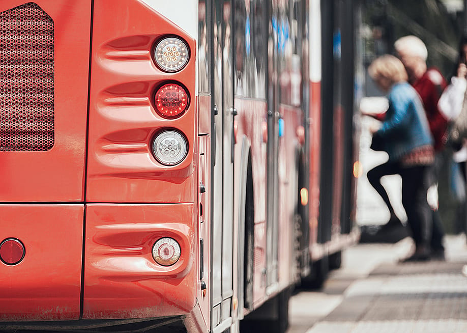 Rear view of a public transport bus at a stop with passengers entering. — AstroStar // Shutterstock