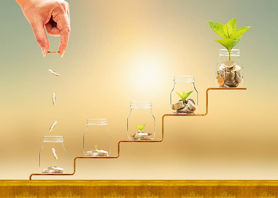 Hand dropping gold coins on jars on a staircase as a concept of financial building. — Watchara Ritjan // Shutterstock