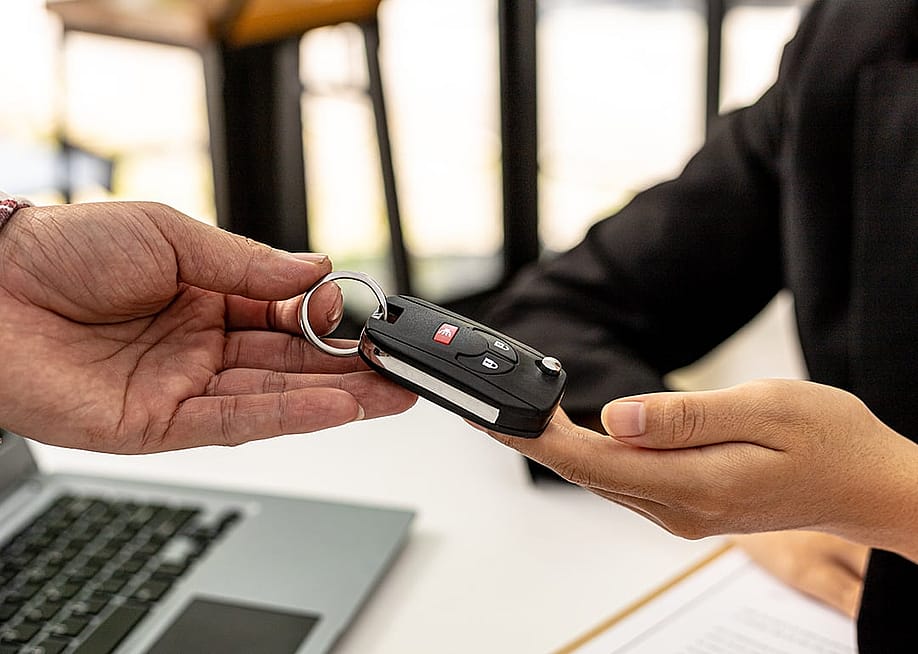 A person returning a car key to an employee for completing a car rental service. — Pickadook // Shutterstock
