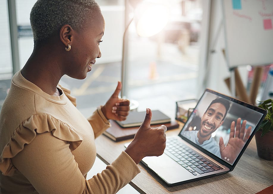 A black woman in an office happily putting two thumbs up during a video call. — PeopleImages