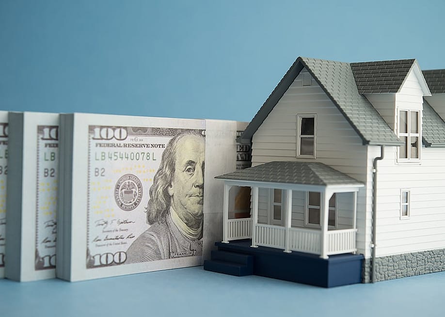 A house miniature and U.S. dollar banknotes in a blue background. — Pla2na // Shutterstock