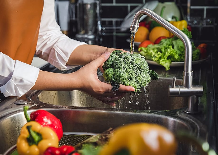 Person washing fresh vegetables over the sink. — Joyseulay // Shutterstock