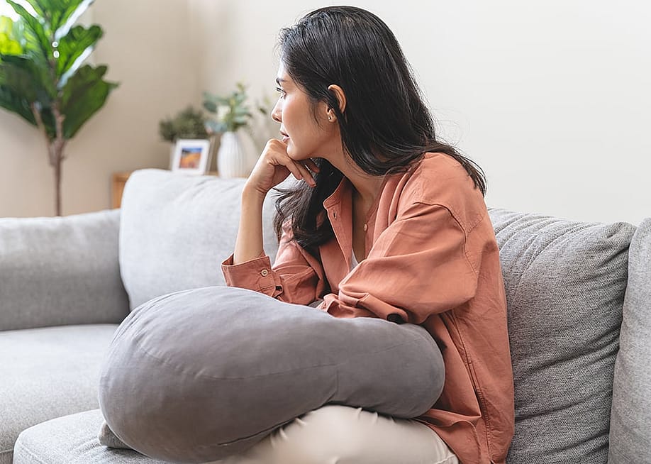 Stressed young woman at home sitting on a sofa. — Pormezz // Shutterstock