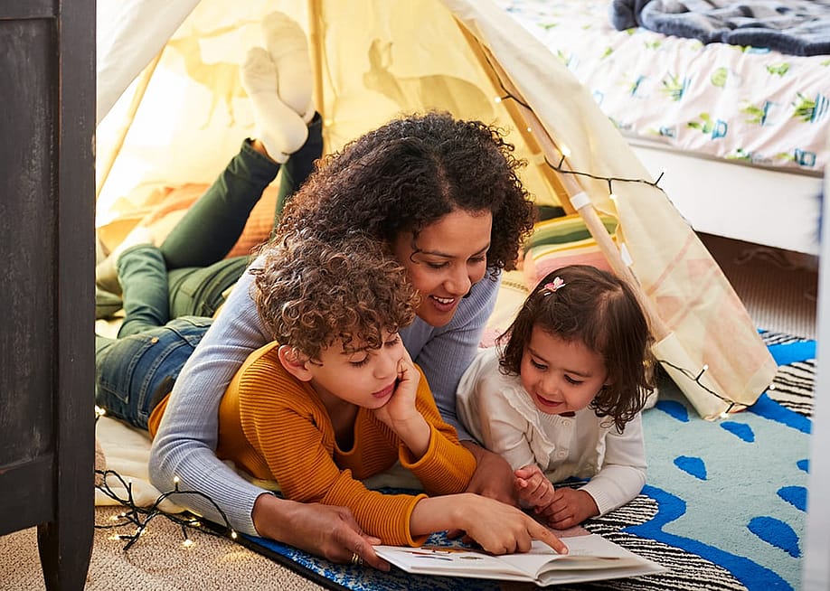 A mother reading a book to his young son and daughter on the floor. — Monkey Business Images // Shutterstock