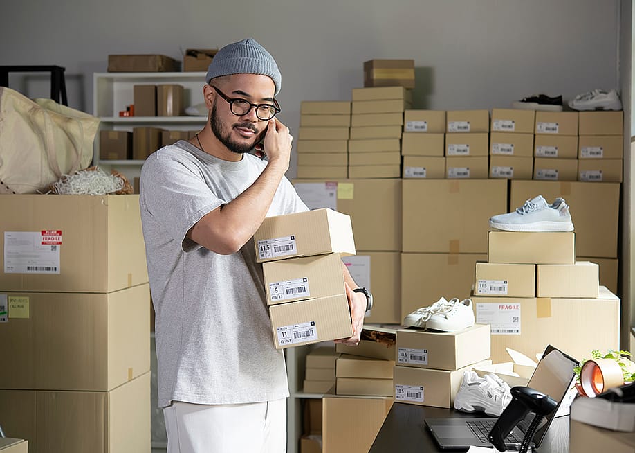 A male e-commerce shoe business owner on the phone while assembling orders. — amenic181 // Shutterstock