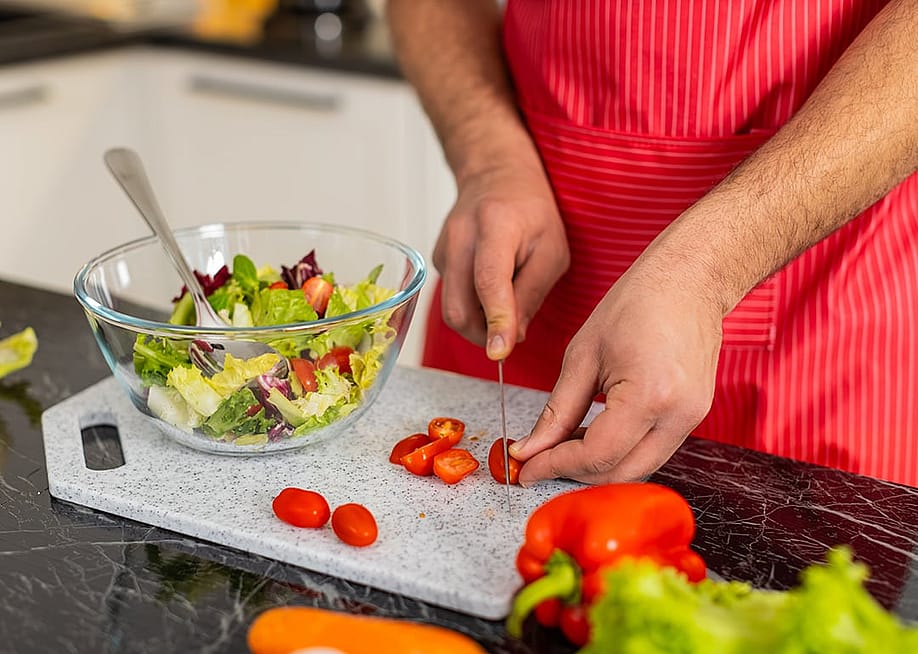 A person slicing cherry tomatoes to a greens salad in the kitchen. — Andrii Iemelianenko // Shutterstock