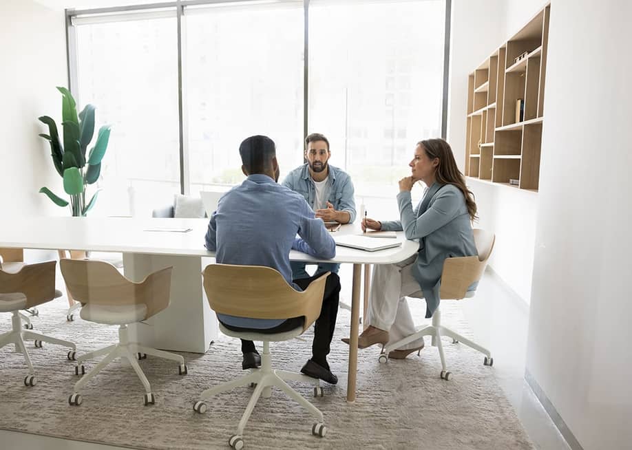 A three-member business team brainstorming inside a meeting room. — fizkes // Shutterstock
