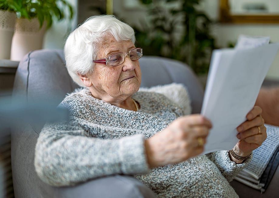 A senior woman reading documents while sitting in an armchair in a living room. — pikselstock // Shutterstock
