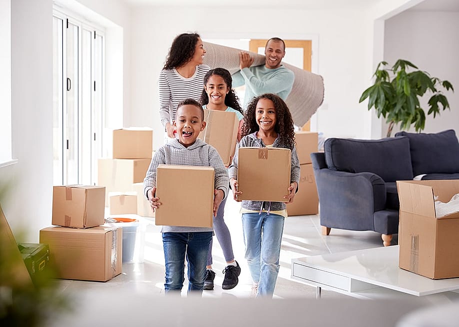 A family of five happily moving boxes into new home. — Monkey Business Images // Shutterstock