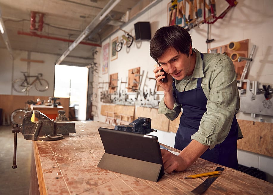A male bicycle small business owner on the phone while reviewing information on a laptop in a workshop. — Monkey Business Images // Shutterstock