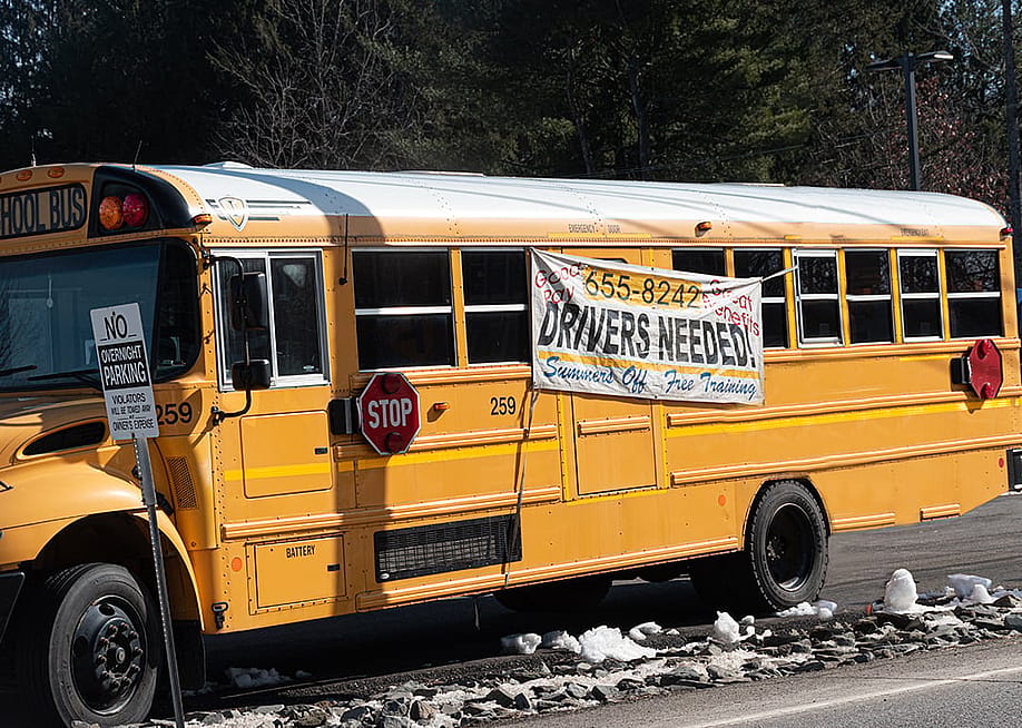 A school bus with a hanging display of drivers needed during a driver shortage in Windsor, New York, USA. — Chet Wiker // Shutterstock