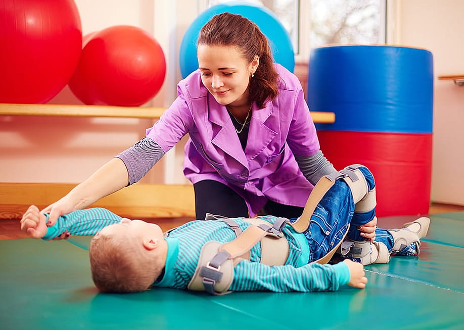 A pediatric therapist helping a young boy with a musculoskeletal therapy exercise. — Olesia Bilkei // Shutterstock