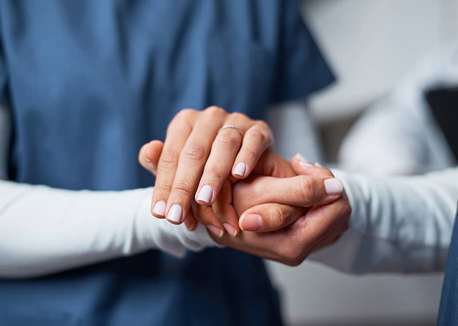 A nurse compassionately holding hand of a patient. — Meeko Media // Shutterstock