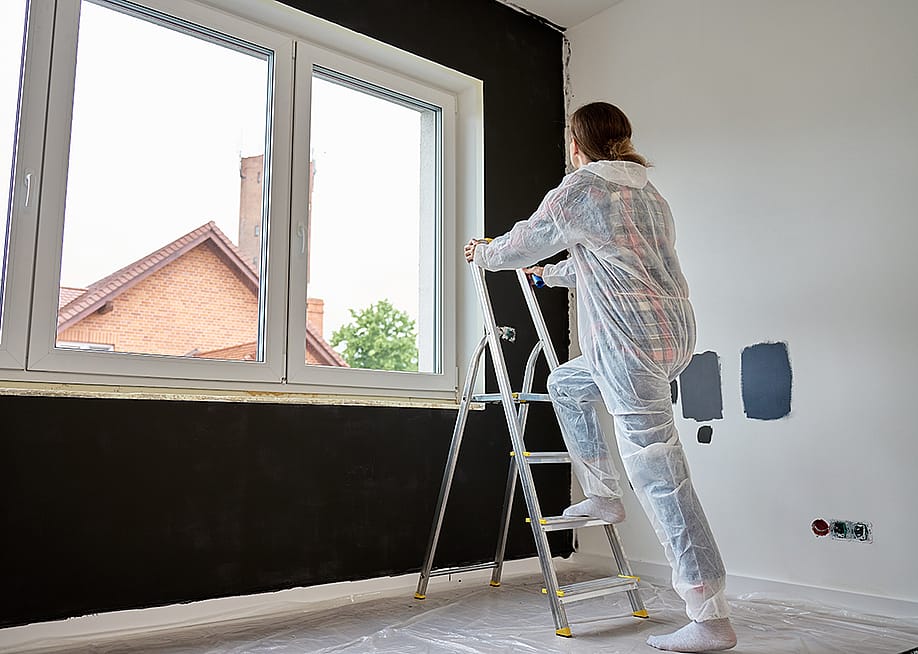Woman in protective wear climbs a ladder to repaint a wall. — Lazy_Bear // Shutterstock