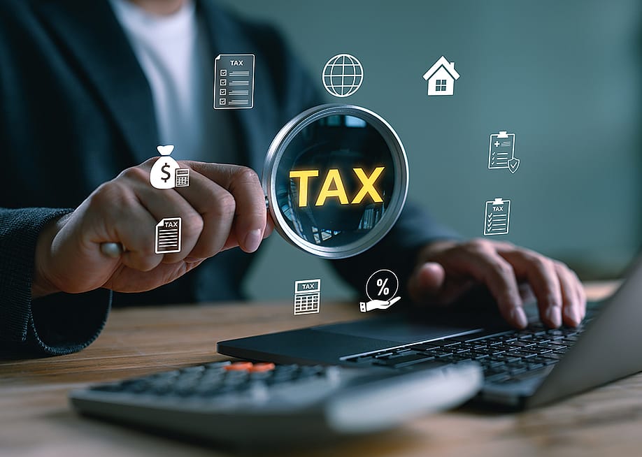 'Tax' and related graphics illustrated over a magnifying glass focusing on a computer as a concept of tax filing. — LookerStudio // Shutterstock