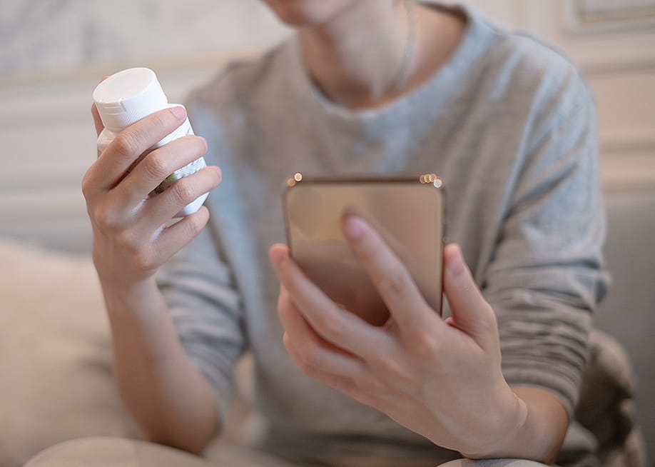 A person holding a vitamin bottle while checking prescription instructions in a smartphone. — Supapich Methaset // Shutterstock
