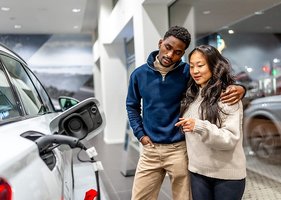 A multiethnic couple examining the charging port of an electric vehicle at a car dealership. — Unai Huizi Photography // Shutterstock