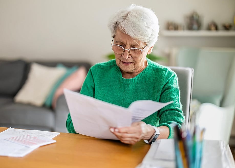 A senior woman sitting in the living room and doing paperwork. — pikselstock // Shutterstock