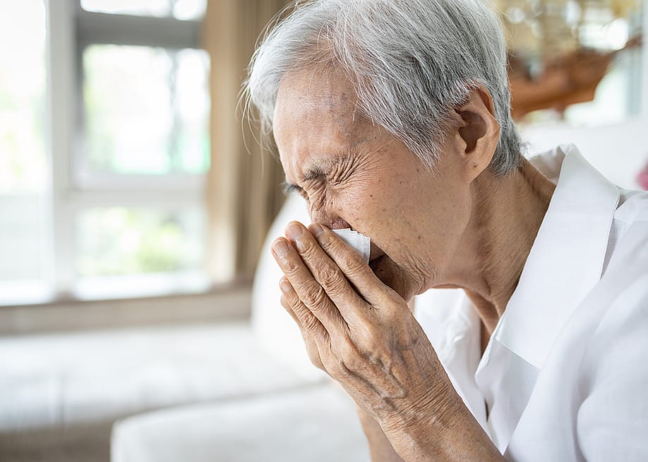 An elderly person blowing her nose after a sneeze. — CGN089 // Shutterstock