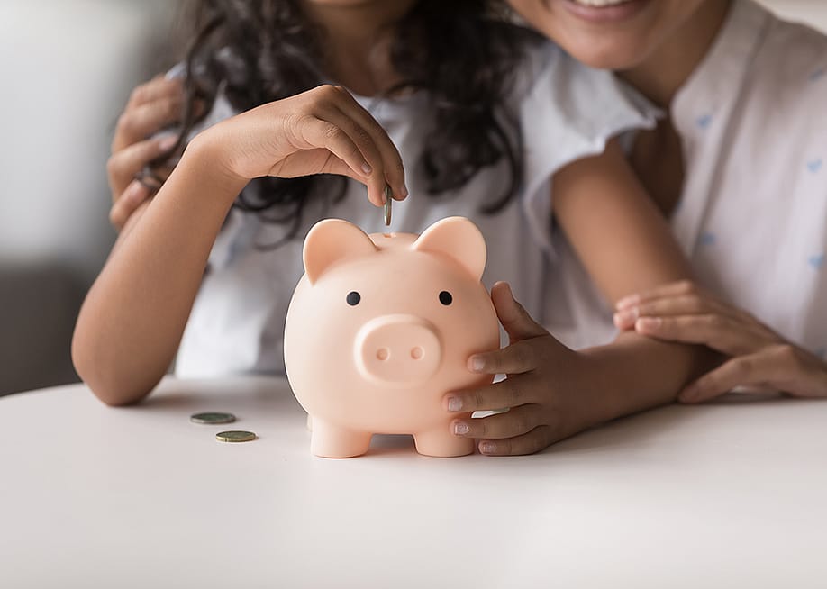 Mother helps daughter put coins in a piggy bank. — fizkes // Shutterstock