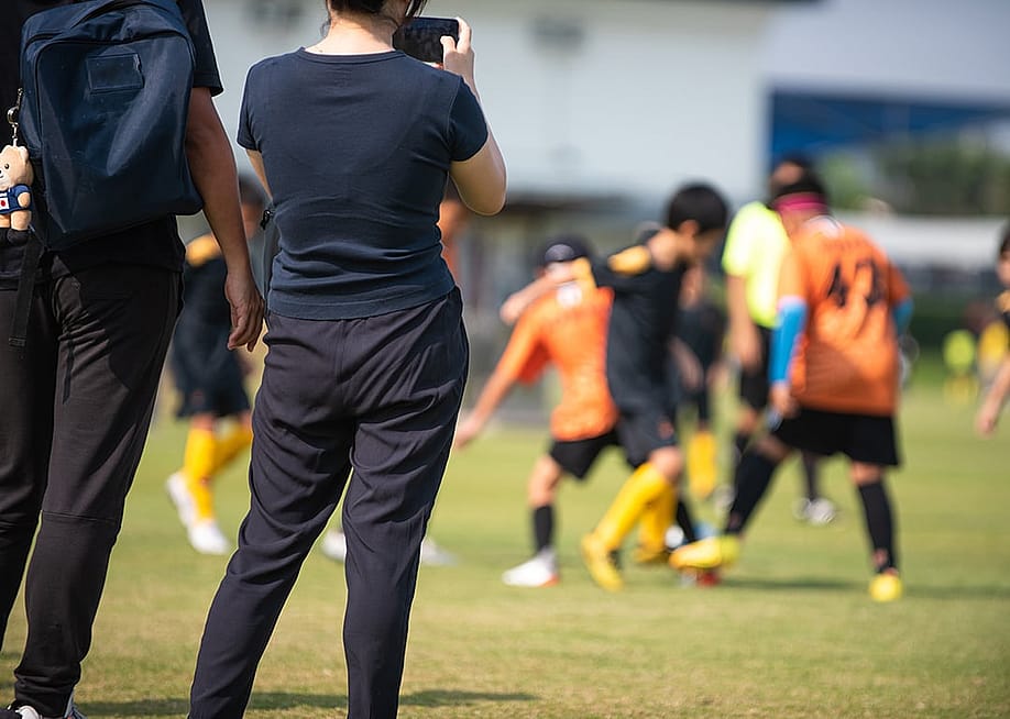 Soccer parents recording their children in a school tournament. — athichoke pim // Shutterstock
